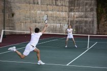 Vue arrière d'une jeune femme caucasienne et d'un homme jouant au tennis, homme retournant la balle avec un mur en arrière-plan — Photo de stock