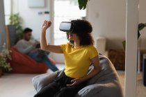 Front view of a young mixed race woman using a VR headset and a young mixed race man sitting in the background at a creative office — Stock Photo
