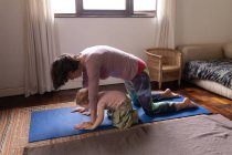 Vista lateral de uma jovem mãe caucasiana em uma pose de ioga ao lado de seu bebê — Fotografia de Stock