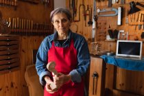 Портрет старших кавказьких жіночих лютьє проведення прокрутки скрипки в її майстерні, з ноутбуком комп'ютер і інструменти висить на стіні у фоновому режимі — стокове фото