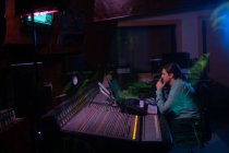 Vista laterale di un giovane ingegnere del suono caucasico seduto e che lavora in un mixer in uno studio di registrazione — Foto stock
