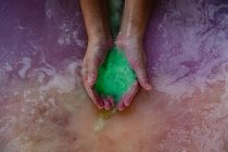 Close-up das mãos de uma mulher em um banho segurando efervescente sais de banho verdes na água do banho rosa — Fotografia de Stock