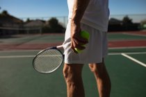 Vista lateral close-up de homem jogando tênis em um dia ensolarado, segurando uma raquete e bolas — Fotografia de Stock