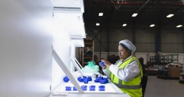 Vista lateral de uma jovem trabalhadora da fábrica afro-americana sentada e inspecionando peças plásticas sob luz brilhante em um armazém em uma fábrica — Fotografia de Stock