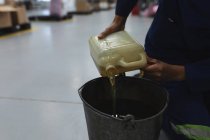 Visão lateral seção média de um trabalhador da fábrica masculino derramando fluido de um recipiente de plástico para um balde em um armazém em uma fábrica de processamento — Fotografia de Stock