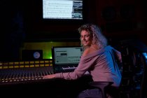Veduta posteriore di una giovane ingegnere del suono caucasica seduta e che lavora ad un mixer in uno studio di registrazione girando e sorridendo alla telecamera — Foto stock