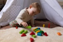 Front view close up of a Caucasian baby sitting on a floor and playing with wooden blocks, barefoot — Stock Photo