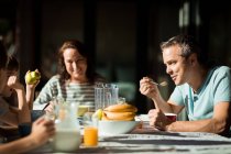 Передній вигляд, близько середнього віку Кавказький чоловік і жінка сидять за столом зі своїми двома передпідлітковими синами, насолоджуючись сімейним сніданком в саду. — стокове фото