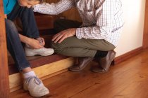 Вид сбоку на белого мужчину средних лет, сидящего на лестнице со своим сыном-подростком, мальчик завязывает шнурки — стоковое фото