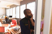 Vista frontal de cerca de un joven afroamericano leyendo notas en una pared y pensando durante una sesión de lluvia de ideas en equipo en una oficina creativa - foto de stock