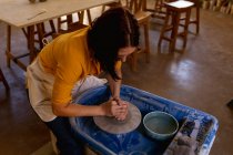 Vista elevada de uma jovem oleiro caucasiana sentada e trabalhando com argila em uma roda de oleiros em um estúdio de cerâmica — Fotografia de Stock