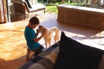 Vista lateral de um menino pré-adolescente caucasiano abraçando um cão em uma sala de estar — Fotografia de Stock
