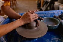 Close up of the hands of female potter shaping wet clay on a potters wheel in a pottery studio — Stock Photo