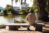 Visão traseira de uma mulher caucasiana sênior sentada em um banco perto de um lago — Fotografia de Stock
