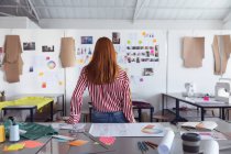 Visão traseira de uma jovem estudante de moda caucasiana olhando para desenhos na parede enquanto trabalhava em um projeto olhando para projetos em uma parede em um estúdio na faculdade de moda — Fotografia de Stock