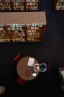 Вид сверху на молодую азиатскую студентку в тюрбане с помощью ноутбука и учебы в библиотеке — стоковое фото