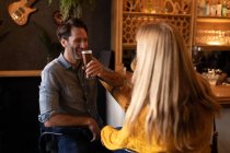 Вид на щасливу молоду Кавказьку пару разом відпочиваючи на відпочинку в барі, питне пиво, вино і посміхається — стокове фото