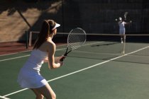 Rückansicht einer jungen kaukasischen Frau und eines Mannes, die an einem sonnigen Tag Tennis spielen, während ein Mann einen Ball schlägt — Stockfoto