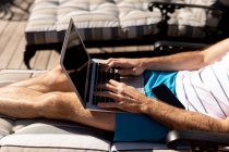 Seitenansicht Mittelteil des Mannes entspannt im Urlaub, auf einer Sonnenliege liegend und mit einem Laptop — Stockfoto