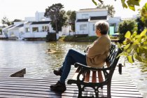 Vista lateral de uma mulher caucasiana sênior sentada em um banco perto de um lago — Fotografia de Stock