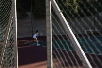 Бічний вид на молоду кавказьку жінку, що грає в теніс, тримаючи ракетку і очікуючи м'яч, побачений через паркан. — стокове фото