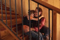 Вид спереди на белую женщину средних лет, обнимающуюся со своим сыном-подростком, сидящим на лестнице — стоковое фото