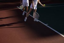 Вид сбоку женщины и мужчины, играющих в теннис в солнечный день, женщина готовится к подаче — стоковое фото