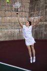 Vue de face d'une jeune femme caucasienne jouant au tennis, tenant une raquette et sautant à la balle avec un mur derrière elle — Photo de stock