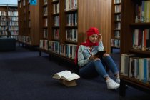 Вид спереди на молодую азиатскую студентку в тюрбане, которая пользуется планшетным компьютером и учится в библиотеке — стоковое фото