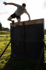 Frontansicht eines jungen kaukasischen Mannes, der während eines Bootcamp-Trainings in einem Outdoor-Fitnessstudio von einer Wand springt — Stockfoto