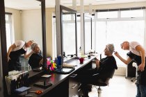 Бічний вид на кавказьку перукарку середнього віку і молоду кавказьку жінку, яка фарбувала волосся в салон для волосся, відображений у дзеркалі. — стокове фото