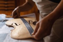 Close up of female luthier measuring the body of a violin on a workbench in her workshop — Stock Photo