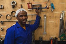 Retrato de perto de um jovem trabalhador da fábrica afro-americano sorrindo para a câmera e buscando uma ferramenta na loja de máquinas em uma fábrica de processamento — Fotografia de Stock