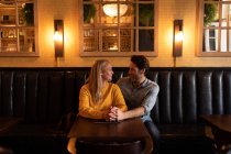 Vista frontale di una giovane coppia caucasica felice che si rilassa insieme in vacanza in un bar, abbracciandosi e tenendosi per mano — Foto stock