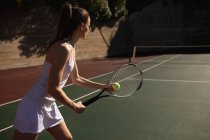 Vista laterale di una giovane donna caucasica che gioca a tennis in una giornata di sole, preparandosi a servire con un muro dietro di lei — Foto stock