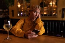 Vorderansicht einer jungen kaukasischen Frau, die sich im Urlaub in einer Bar entspannt, Wein trinkt und ein Smartphone benutzt — Stockfoto
