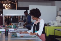 Seitenansicht einer jungen Studentin mit gemischter Rasse, die in einem Studio der Modehochschule an einem Design arbeitet, während ein männlicher Student im Hintergrund arbeitet — Stockfoto