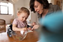 Side view close up of a young Caucasian mother coloring with her baby, sitting at a table — Stock Photo
