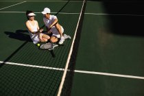 Front view of a young Caucasian woman and a man talking and using a smartphone at a tennis court on a sunny day — Stock Photo