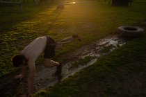 Вид збоку молодого Кавказького чоловіка, що тягне шину на мотузці навколо талії через бруд, що падає на відкритий тренажерний зал під час тренування Bootcamp — стокове фото