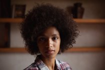 Портрет крупным планом молодой женщины смешанной расы в клетчатой рубашке, смотрящей прямо в камеру дома — стоковое фото
