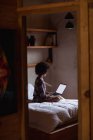 Seitenansicht einer jungen Mischlingshündin mit einem Laptop, die zu Hause auf ihrem Bett sitzt und sich im Spiegel ihres Zimmers spiegelt — Stockfoto