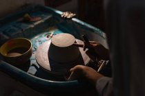 Vue latérale section médiane du potier féminin à l'aide d'un outil pour façonner la base d'un bol sur une roue de potiers dans un atelier de poterie — Photo de stock