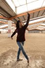 Nahaufnahme einer jungen Balletttänzerin mit gemischter Rasse in Jeans und Spitzenschuhen, die mit ausgestreckten Armen in einer verlassenen Lagerhalle tanzt — Stockfoto