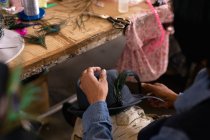 Über die Schulteransicht einer Frau, die in der Werkstatt einer Hutfabrik einen Hut hält und ihm den letzten Schliff verleiht, mit einem Arbeitstisch und Materialien im Hintergrund — Stockfoto