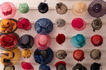 Front view of various styles of hats displayed in rows on the white wall of the showroom at a hat makers — Stock Photo