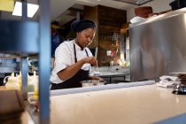 Vue de face gros plan d'une jeune cuisinière afro-américaine préparant à manger dans une casserole dans une cuisine de restaurant — Photo de stock