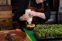 Vista frontal seção média de um jovem cozinheiro branco espremendo molho de uma garrafa em um prato em uma cozinha do restaurante — Fotografia de Stock