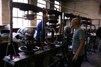 Seitenansicht einer gemischten Rasse älteren und mittleren Alters, die gemeinsam an einer Maschine in der Werkstatt einer Hutfabrik arbeiten — Stockfoto