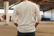 Rear view close up of a young man standing with his hands in his pockets in an empty room at an abandoned warehouse — Stock Photo
